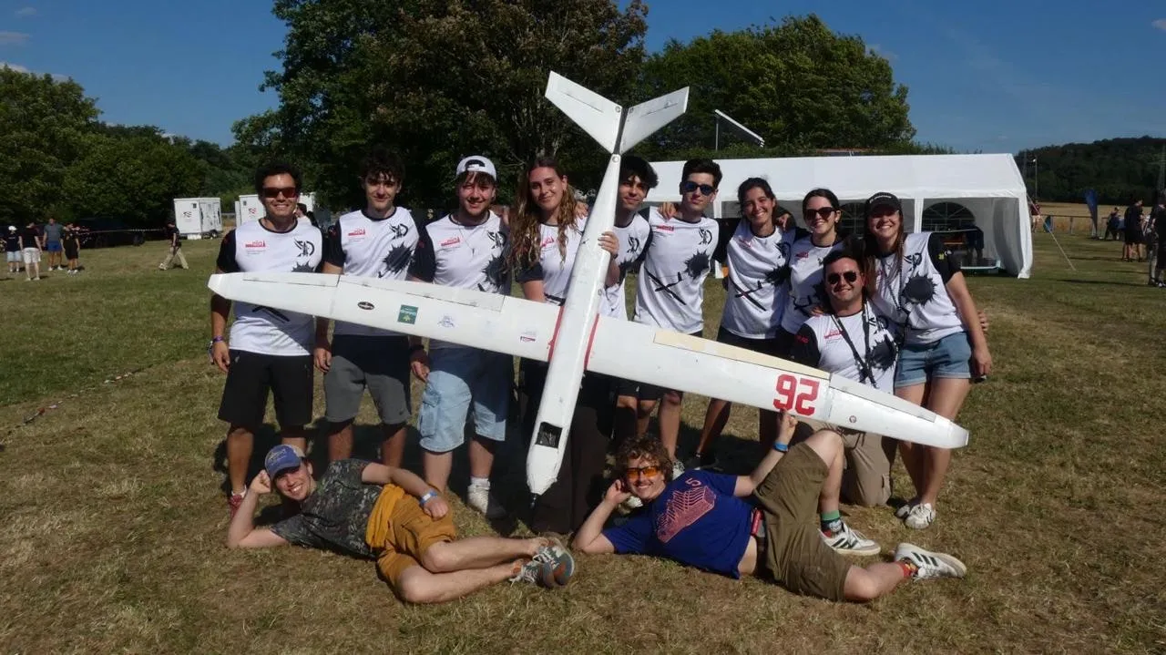 El equipo posa con el avión en el campo de vuelo; dos miembros, tumbados delante.