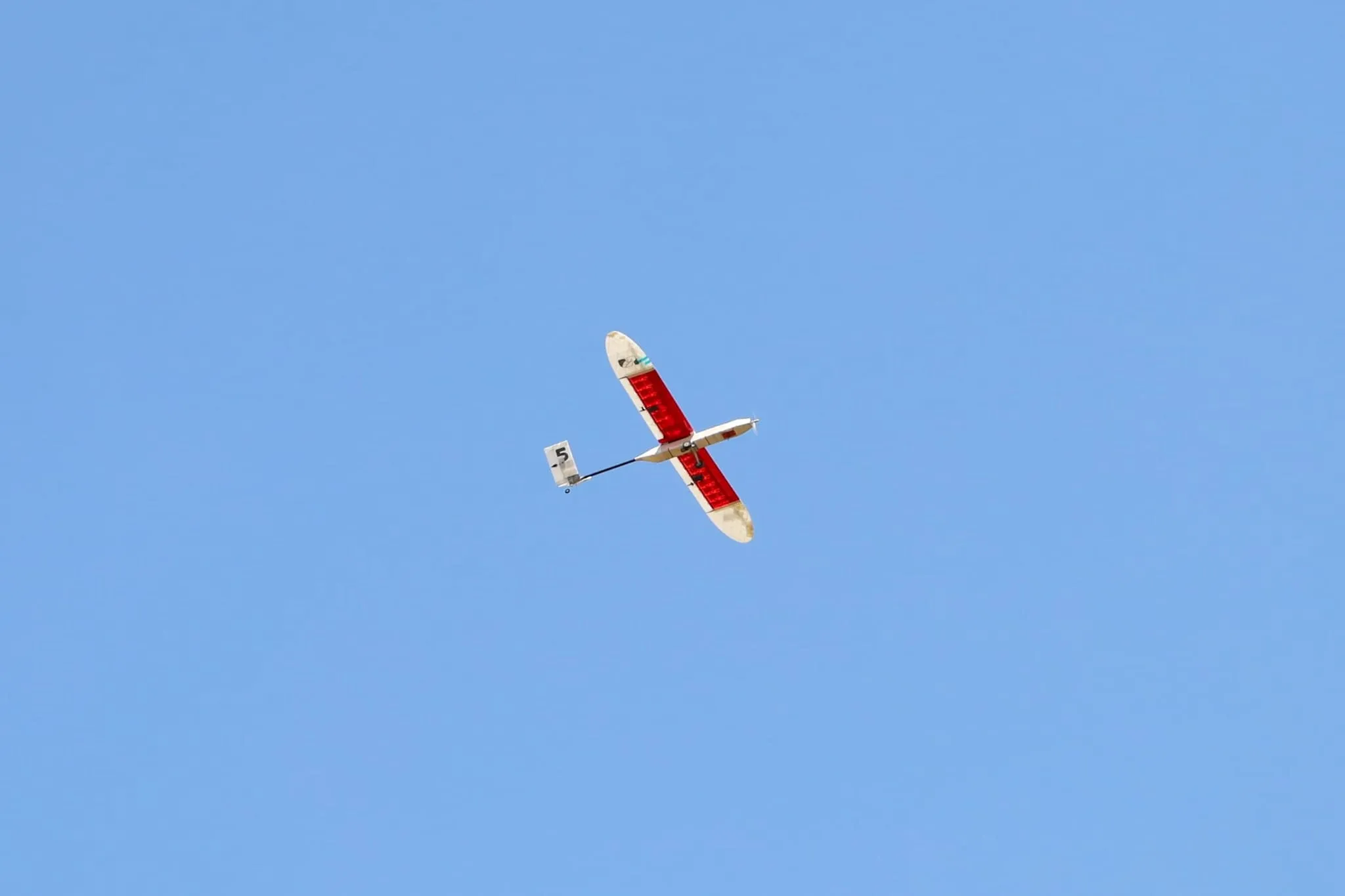 El Aurora en vuelo, visto desde abajo, con el ala roja a contraluz.