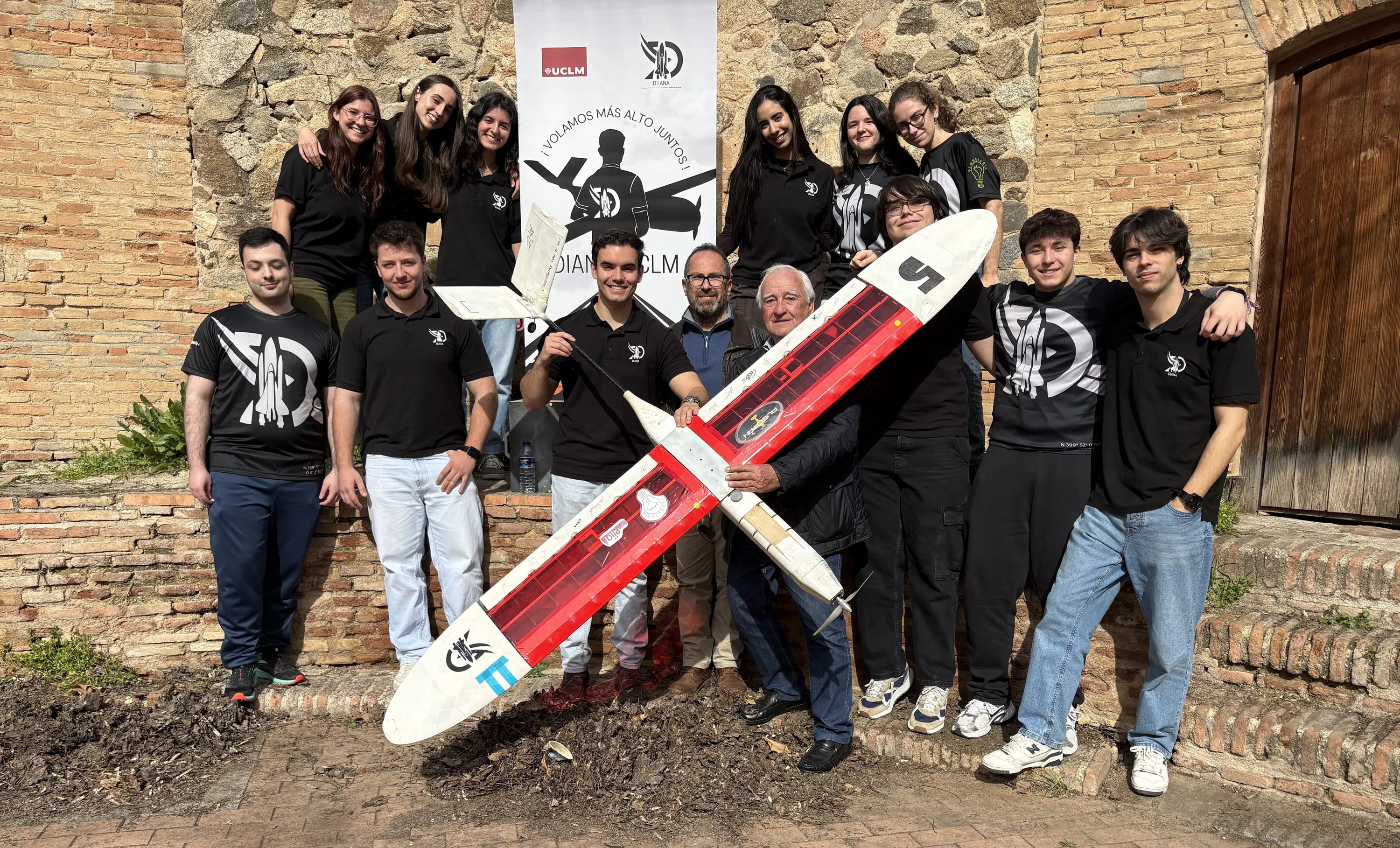 El equipo, unas quince personas, sostiene el Eclipse en diagonal en un patio de ladrillo, con el roll-up de DIANA al fondo.