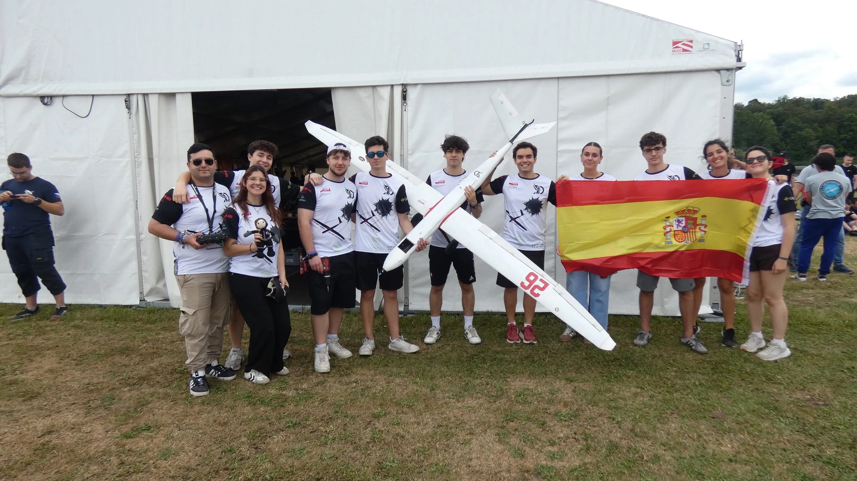 Una docena de miembros con camiseta blanca de DIANA, la bandera de España y el avión, delante de la carpa del Air Cargo Challenge.